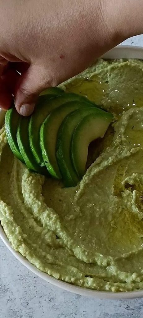 Hummus garnished with avocado, sesame seeds, and oil