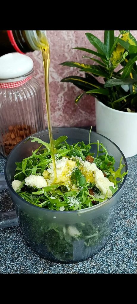 Arugula, almonds, garlic, grated Parmesan, oil in the chopper on dark background
