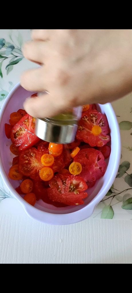 We season the tomatoes with salt, pepper, oregano, and oil