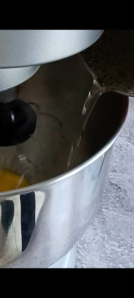 Adding the water and sugar syrup while continuing to whip the yolks