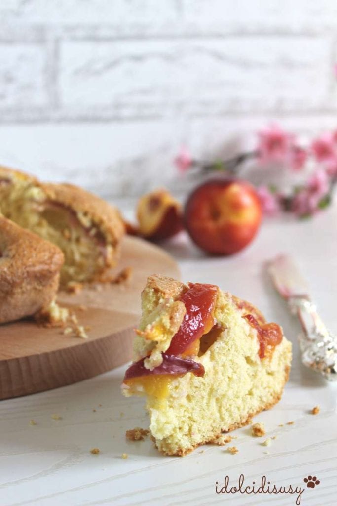 Whole peach cake with a slice in the foreground, on a wooden board