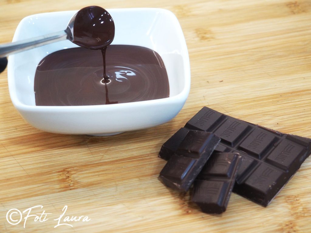Melted chocolate dripping from a teaspoon and solid chocolate cubes on a wooden board