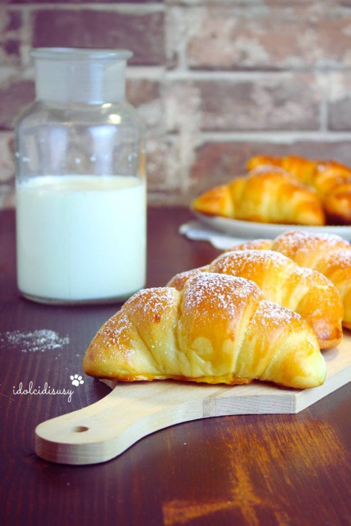 Soft and golden homemade brioches with powdered sugar served on a cutting board with a glass of milk