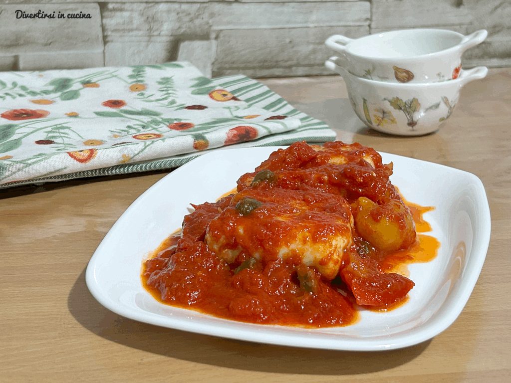 A plate of hake fillets cooked in tomato sauce with red, yellow peppers and capers.