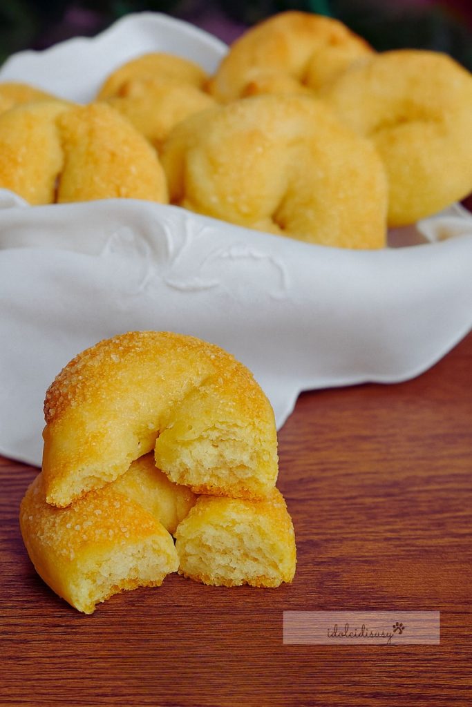 Homemade wine doughnuts broken in half, crunchy outside and crumbly inside, served on a wooden surface with a basket in the background