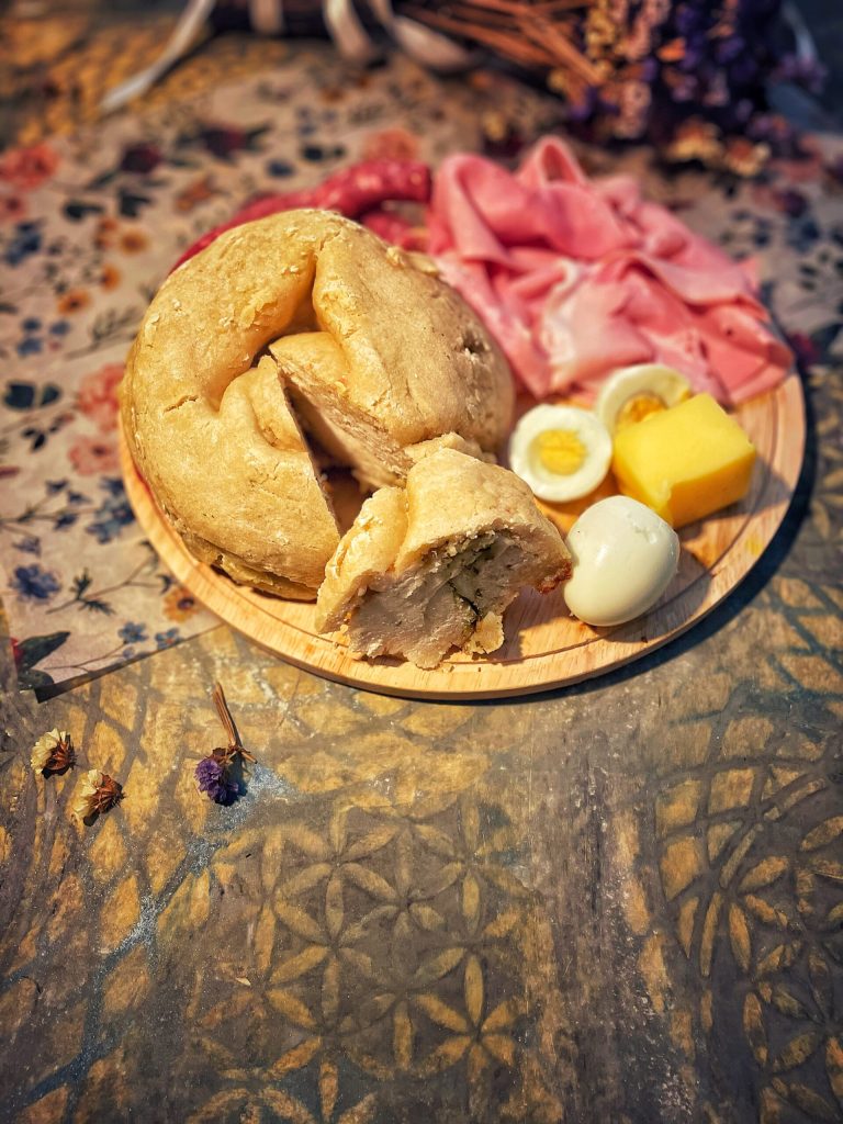 "Wooden board with Carinthian Osterjause: slices of sweet Reindling served along with slices of Osterschinken (Easter ham), boiled eggs, sausage, and butter