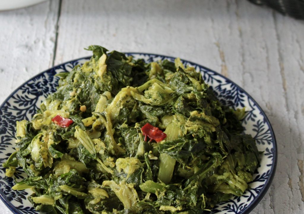 Roman-style sautéed broccoli rabe with garlic, oil, and chili served on a plate with bread in the background