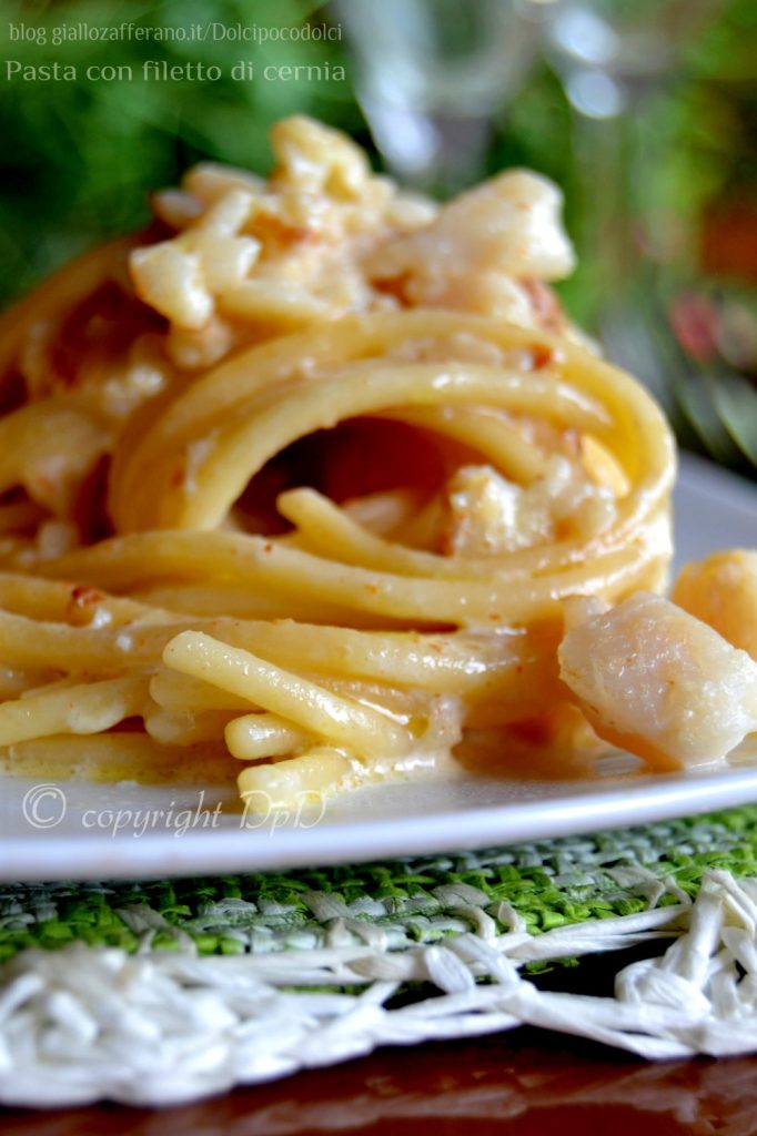 Pasta with grouper fillet served on a white plate, with creamy sauce and pieces of fish