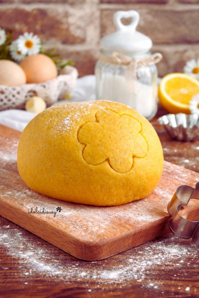 Homemade shortcrust pastry dough on a wooden board with a flower-shaped cutter and flour