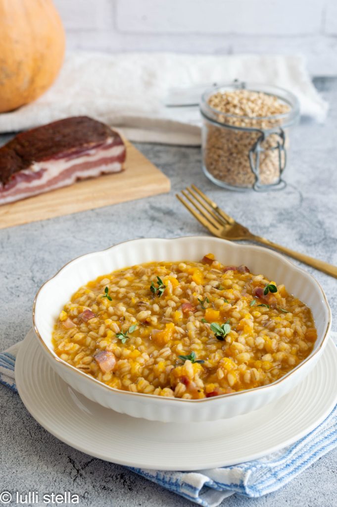 Orzotto with pumpkin and speck on a white plate, creamy and inviting