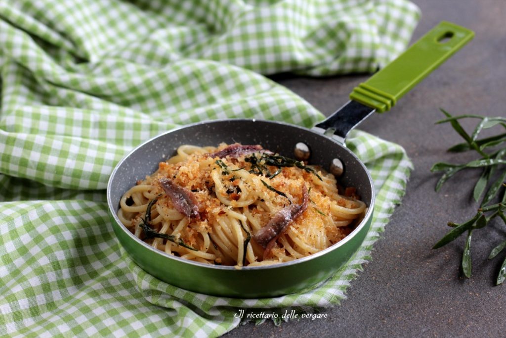 Close-up of a plate of spaghetti with Conero paccasassi, anchovies and crunchy crumbs, served in a small green pan.