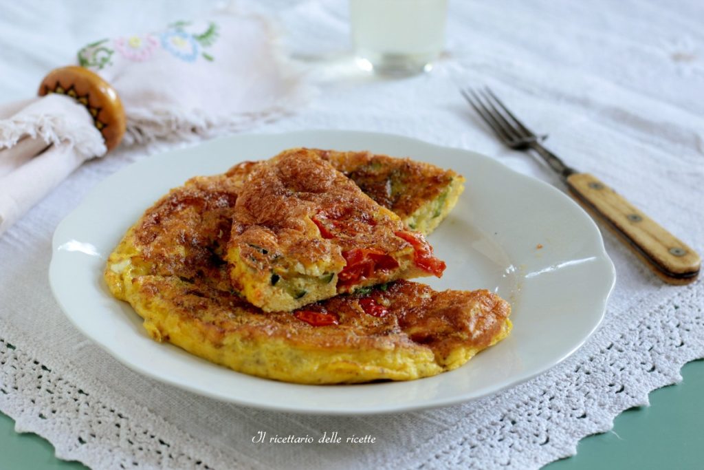 Zucchini and cherry tomato frittata sliced on a white plate with embroidered tablecloth