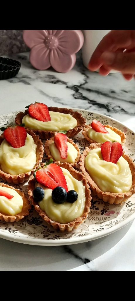 Törtchen gefüllt mit Creme und Früchten auf einem weißen, schwarzen und rosa Teller