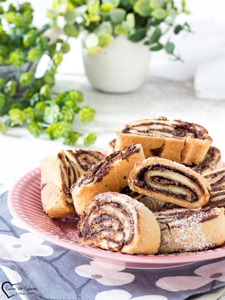 Legen Sie die Mürbeteig- und Haselnussrolle mit dem Backpapier darunter auf das Backblech und backen Sie im vorgeheizten statischen Ofen bei 180°C für 20 Minuten. Wenn sie fertig sind, aus dem Ofen nehmen und vollständig abkühlen lassen. Wenn sie kalt sind, in etwa 1 cm dicke Scheiben schneiden und die Mürbeteig- und Schokoladenkekse servieren.
