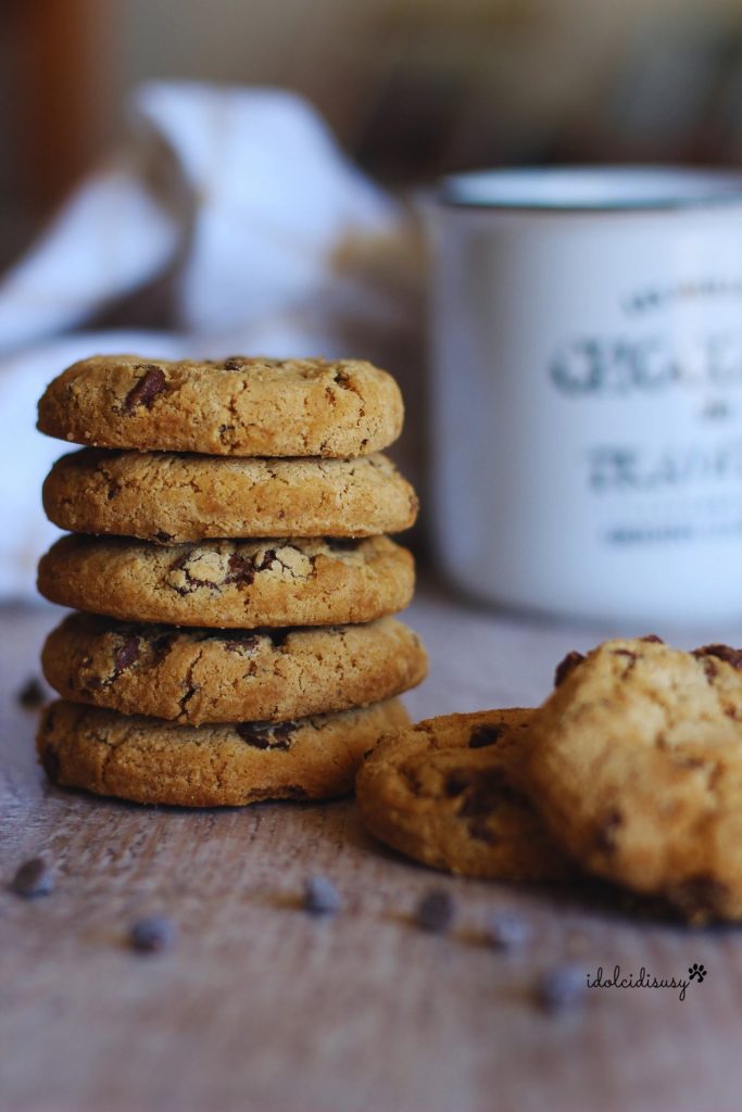 Ein Stapel Cookies mit Schokostückchen auf einer Holzplatte mit einer Tasse im Hintergrund