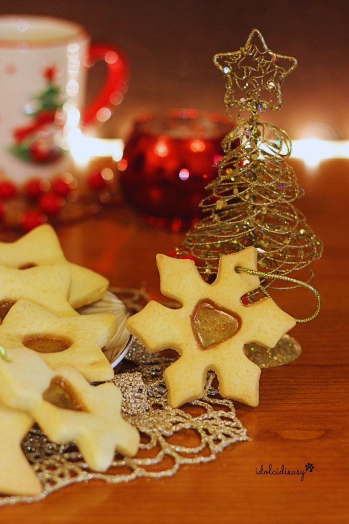 Weihnachtsplätzchen mit Glaseffekt in Form einer Schneeflocke mit transparentem Herz und goldenem Baum im Hintergrund