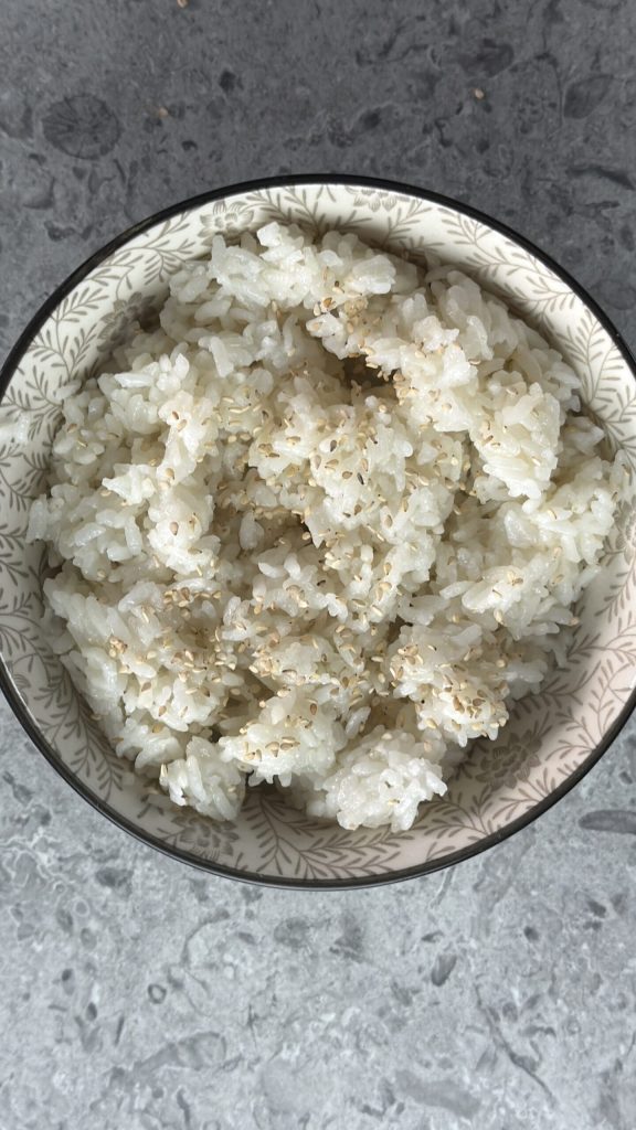Sushi‑Reis in eine Schüssel geben und Sesam bestreuen