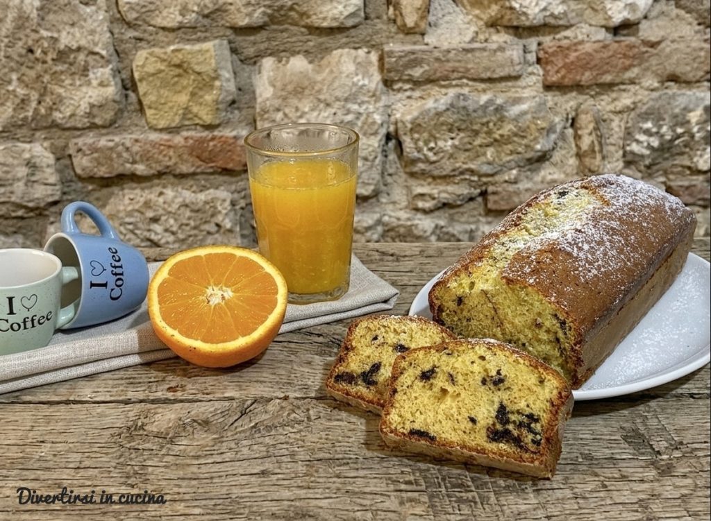Ein Orangengugelhupf mit Schokoladenstückchen, aufgeschnitten auf einem rustikalen Holztisch, begleitet von einem Glas frisch gepresstem Orangensaft und Espressotassen
