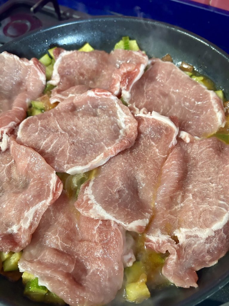 Schweinelendenscheiben zu den Zucchini und Tomaten in der Pfanne gegeben