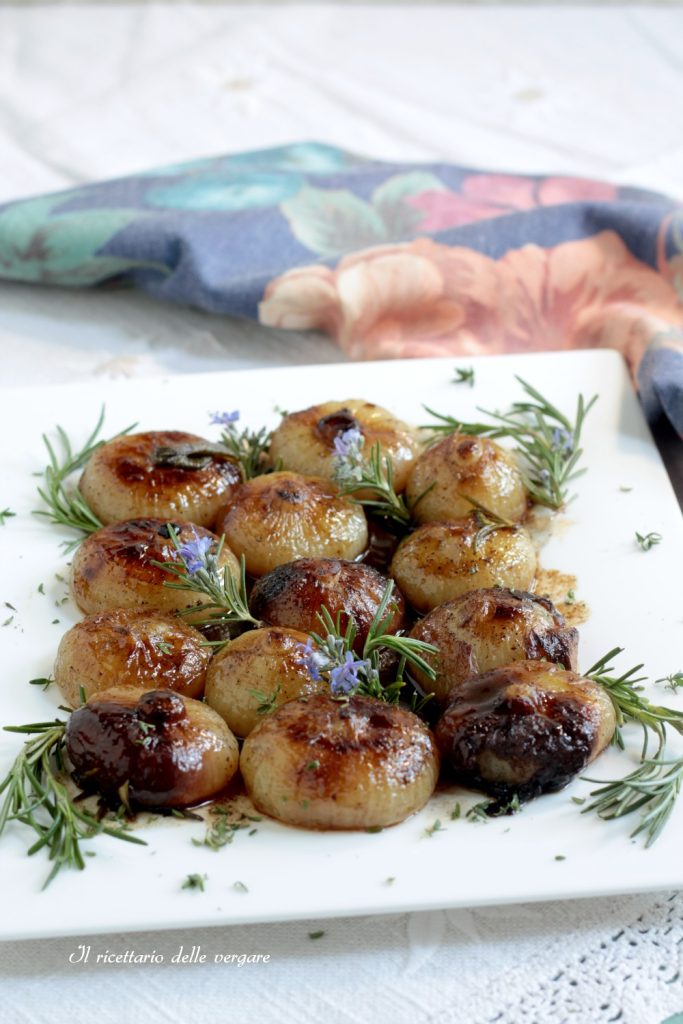 Detailaufnahme von Borettane-Zwiebelchen, gebraten in der Kasserolle, dekoriert mit Rosmarin und Blüten.