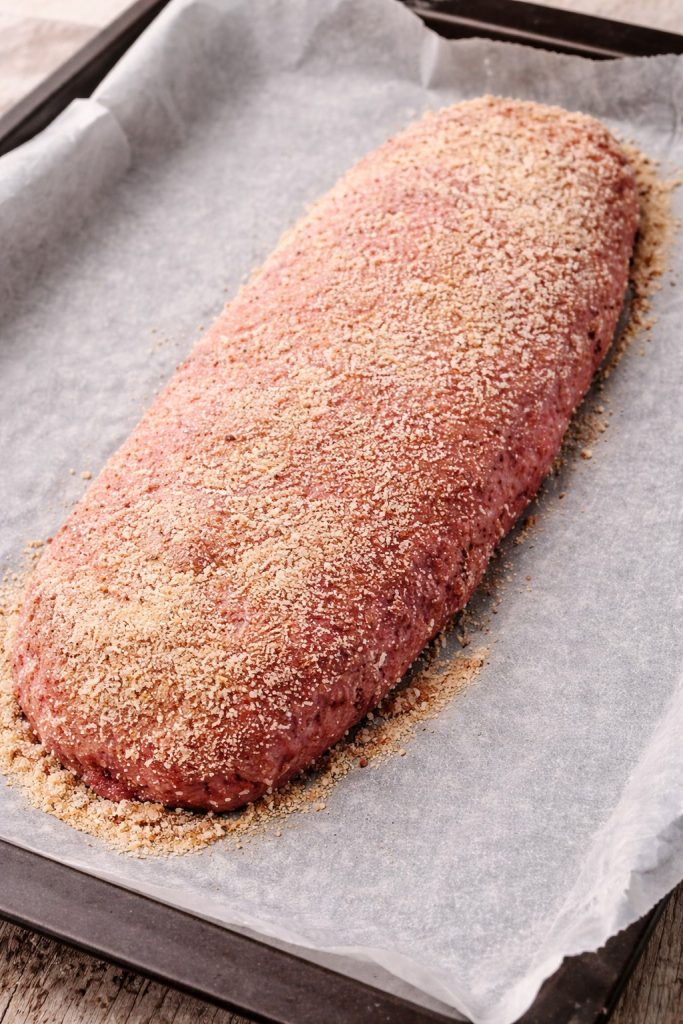 Rohes Hackbratenstück auf Backpapier im Backblech vor dem Backen