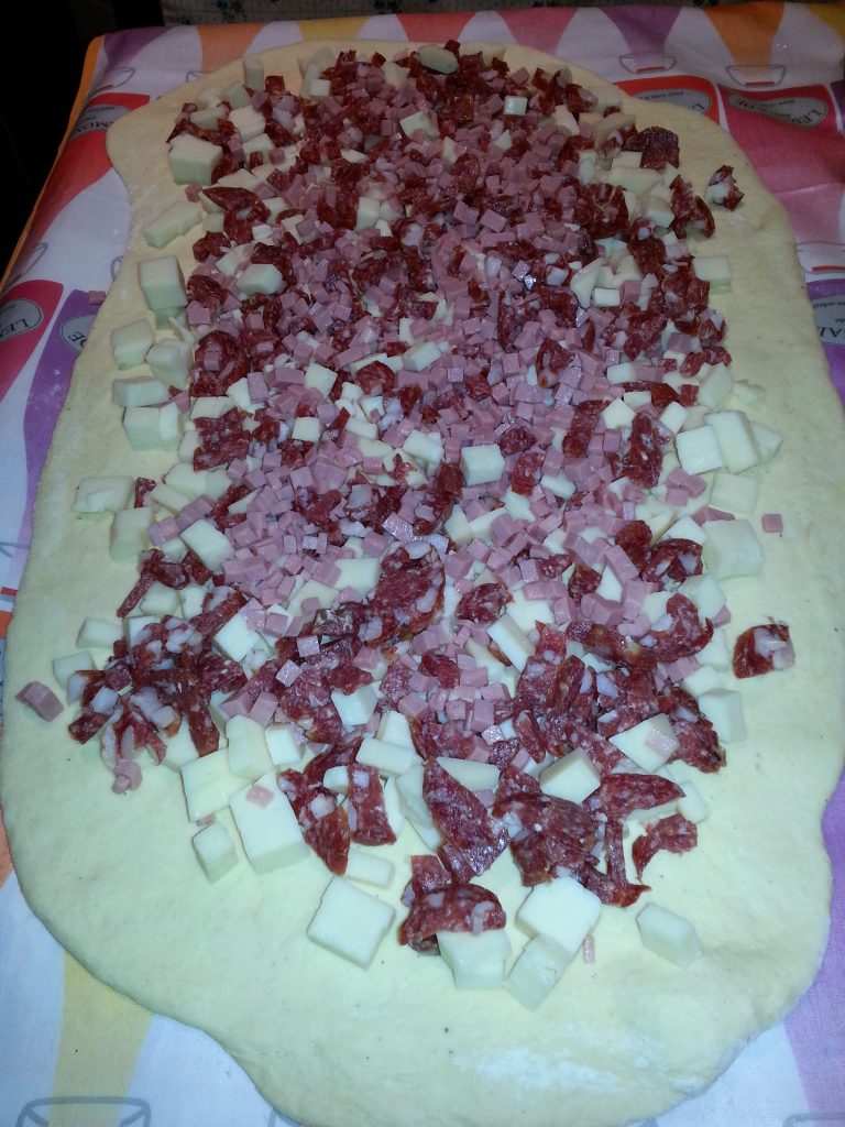 Tortano-Teig ausgebreitet mit gewürfelter Wurst und Käse vor dem Aufrollen