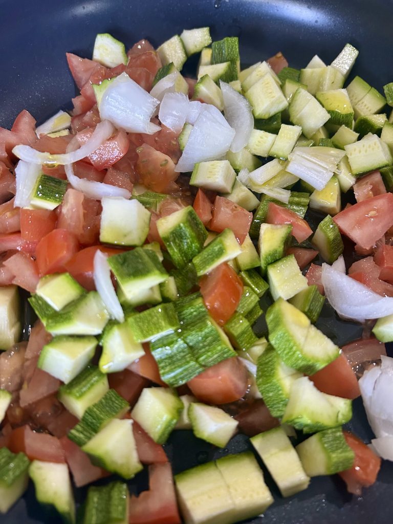 Zucchini und Tomaten beim Braten in der Pfanne mit Zwiebel und Öl
