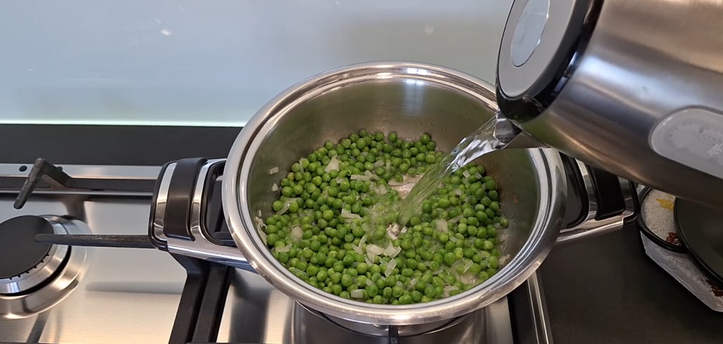 Ajout d'eau chaude dans la casserole avec petits pois et oignon