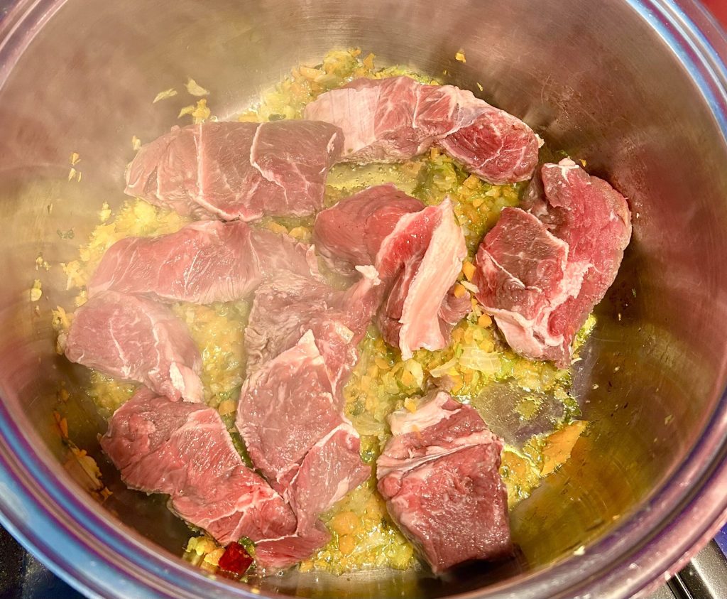 Morceaux de bœuf en train de dorer dans le sofritto de céleri, carotte et oignon pour préparer le ragoût en sauce onctueuse