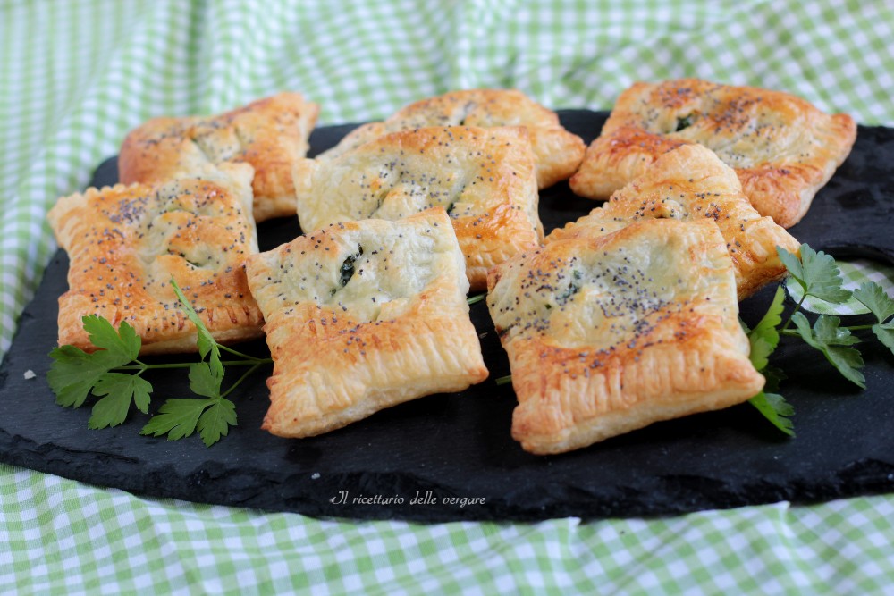 Fagottins de pâte feuilletée dorés, garnis de ricotta et d'épinards, disposés sur une assiette sombre avec des feuilles de jeunes pousses d'épinard fraîches