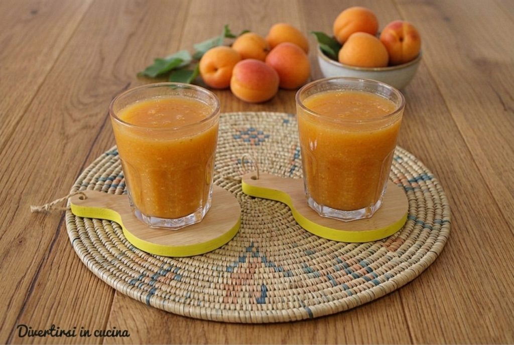 Deux verres de jus d'abricot sur une planche en bois et une nappe tressée, avec des abricots frais en arrière-plan