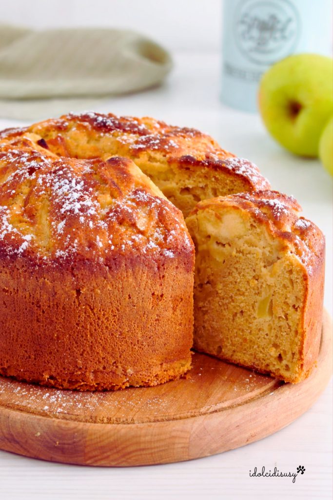 Gâteau aux pommes moelleux au Bimby fait maison, saupoudré de sucre glace et avec des pommes dans la pâte, découpé en tranches sur une planche en bois