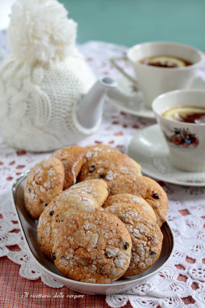 Biscuits moelleux à l'orange avec pépites de chocolat sur un plateau, à côté d'une théière blanche et de tasses de thé.