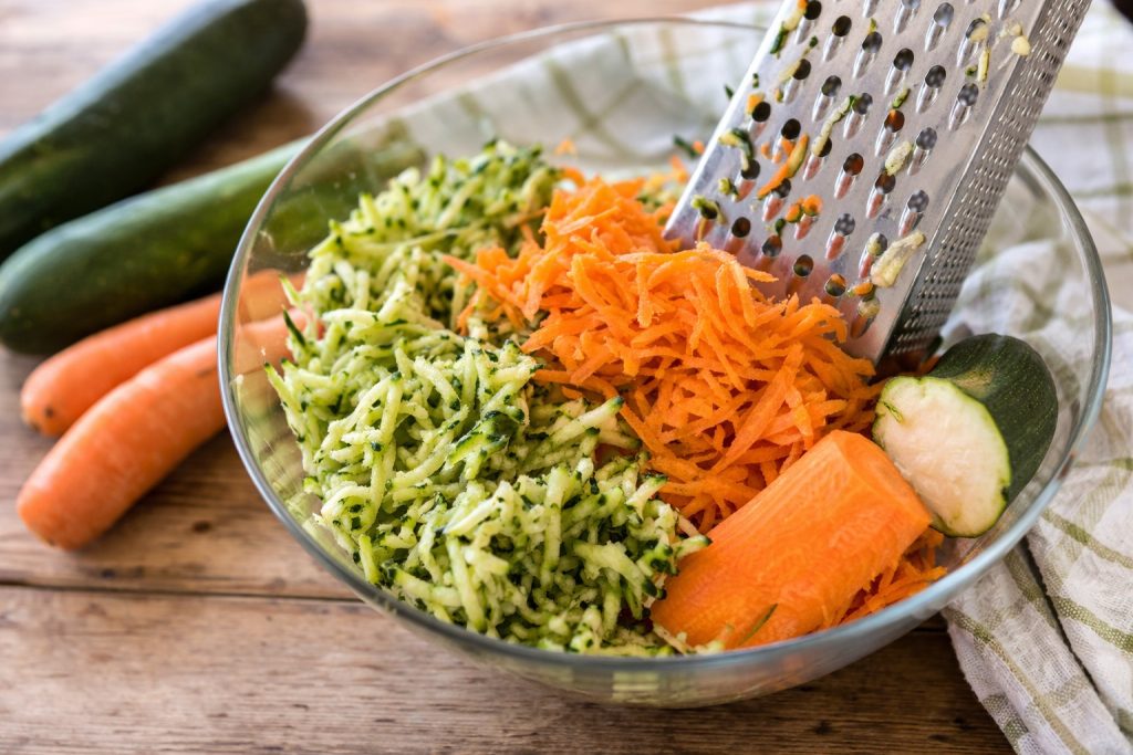 courgettes et carottes râpées dans un bol avec une râpe à gros trous
