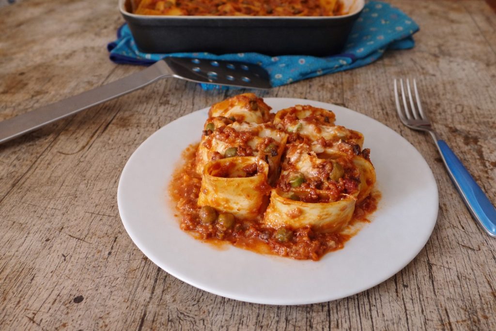 portion de paccheri gratinés au four avec ragù et petits pois dans l'assiette, vue rapprochée