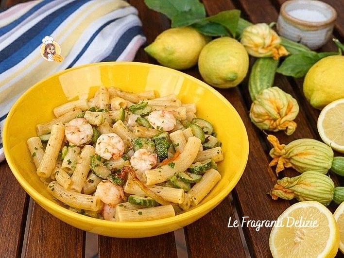 Pâtes aux crevettes, courgettes et fleurs de courgette servies dans une assiette jaune sur une table en bois en plein air