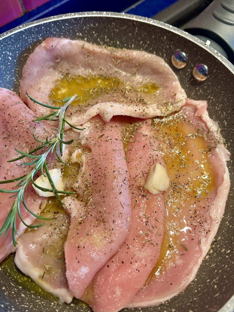 tranches de filet de porc crues assaisonnées d'huile, romarin, ail et poivre dans la poêle