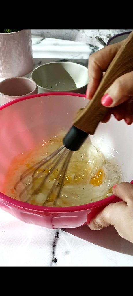 Huevos, leche, yogur, aceite en bol rosa mezclados con varilla