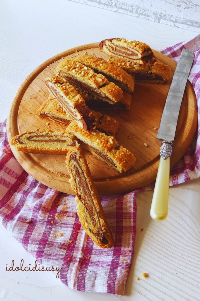 Rodajas de rollo de masa quebrada con chocolate colocadas en una tabla con cuchillo y mantel rosa
