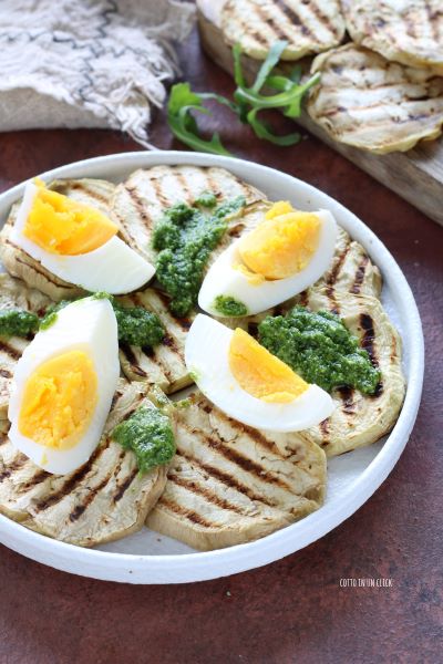 distribuye las berenjenas en un plato, añade los huevos cortados y condimenta con pesto de rúcula