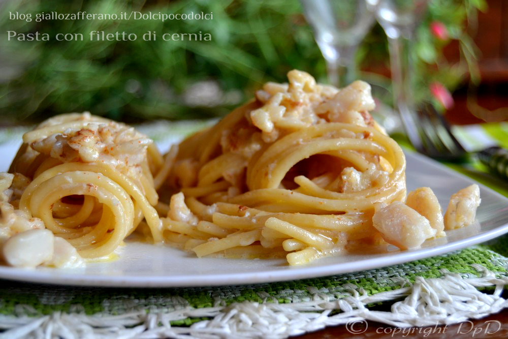 Pasta con filete de mero servida en plato blanco, con salsa cremosa y pescado en trozos