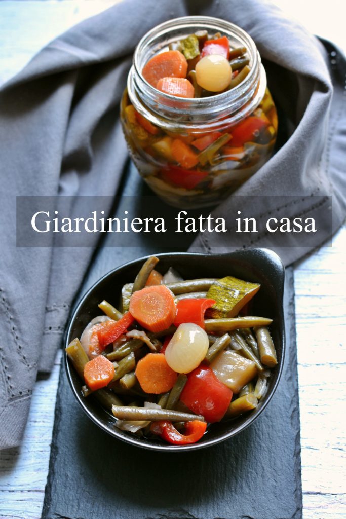 Giardiniera en agridulce en cuenco oscuro y tarro de vidrio sobre superficie de pizarra, con verduras variadas y coloridas
