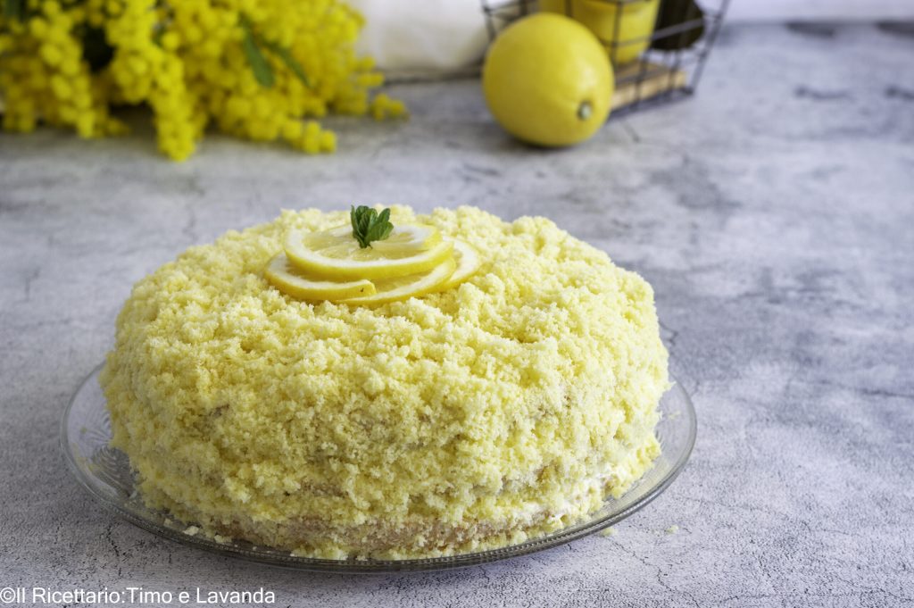 Tarta mimosa de limón sin gluten y sin lactosa decorada con cubitos de bizcocho y crema de limón, vista frontal en plato de vidrio