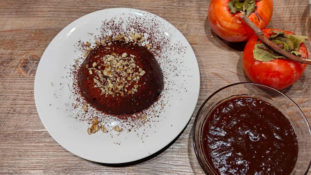 ⏳ El reposo: la clave para un pudín sin cocción impecable. Una vez que tengas tu crema de chocolate 100% natural, viértela en los moldes o en las copas para pudín. El reposo en la nevera durante al menos dos horas es fundamental, porque es durante ese tiempo cuando la pulpa del caqui libera su capacidad espesante natural. Para una mise en place impecable o para organizarte mejor, también puedes preparar tu postre rápido la noche anterior. 🍓 Toque final: decoración Al servir tu Pudín de Caqui sin Azúcar, no te saltes la decoración. Un toque de cacao amargo espolvoreado en la superficie y un puñado de pistachos picados no solo añaden un contraste cromático perfecto (food styling), sino que su crujiente casa magníficamente con la cremosidad del pudín, elevando la experiencia gustativa de tu postre sencillo. Una alternativa espectacular es usar granillo de avellanas o frambuesas frescas.