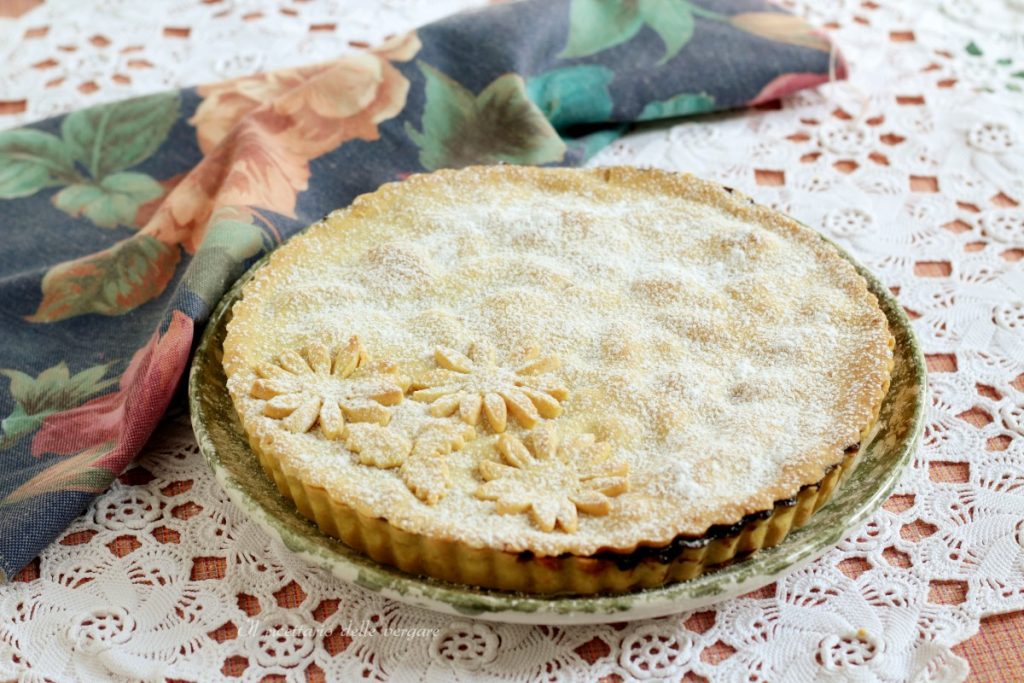 Crostata cubierta dorada con relleno de cerezas y manzanas, espolvoreada con azúcar glas sobre una mesa puesta.