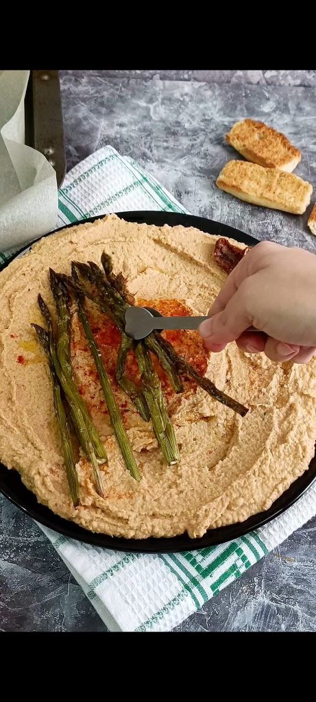 Prato preto em fundo cinza com hummus e aspargos