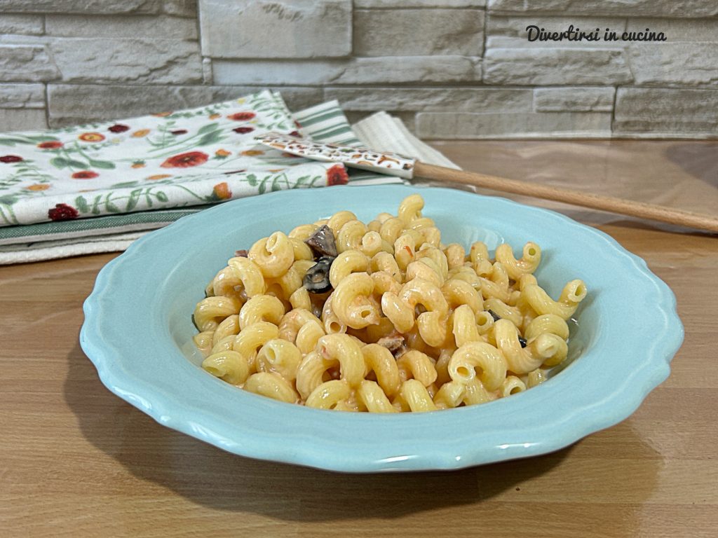 Massa cremosa com tomatinhos, molho branco, bacon crocante e azeitonas pretas, servida em um prato azul.