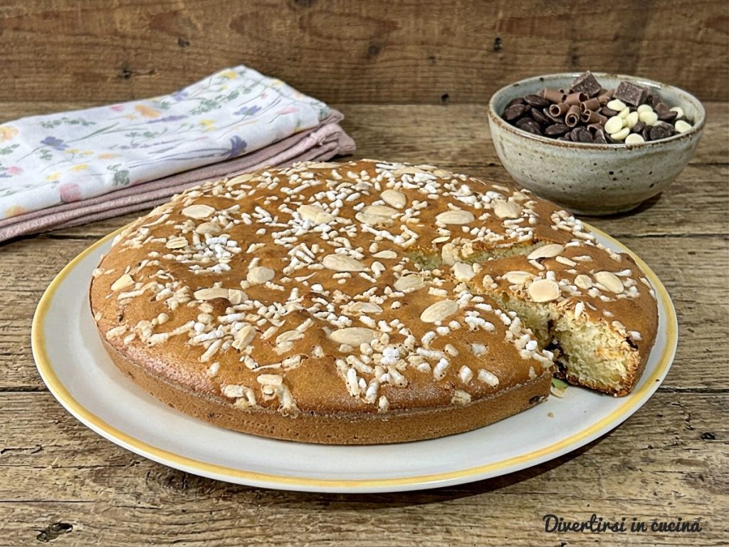 Bolo fofinho de amaretto com amêndoas e açúcar granulado sobre uma tábua rústica de madeira, ao lado de uma tigela com chocolate misto.