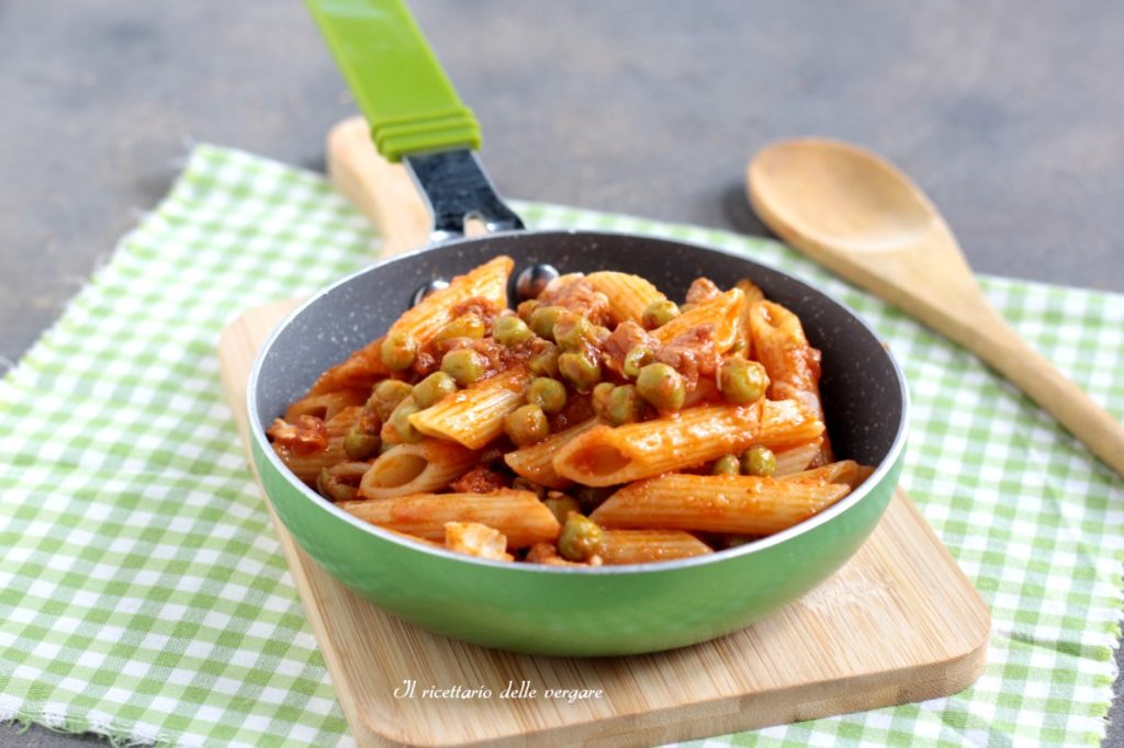 Frigideira verde com penne ao molho de tomate e ervilhas sobre tábua de madeira