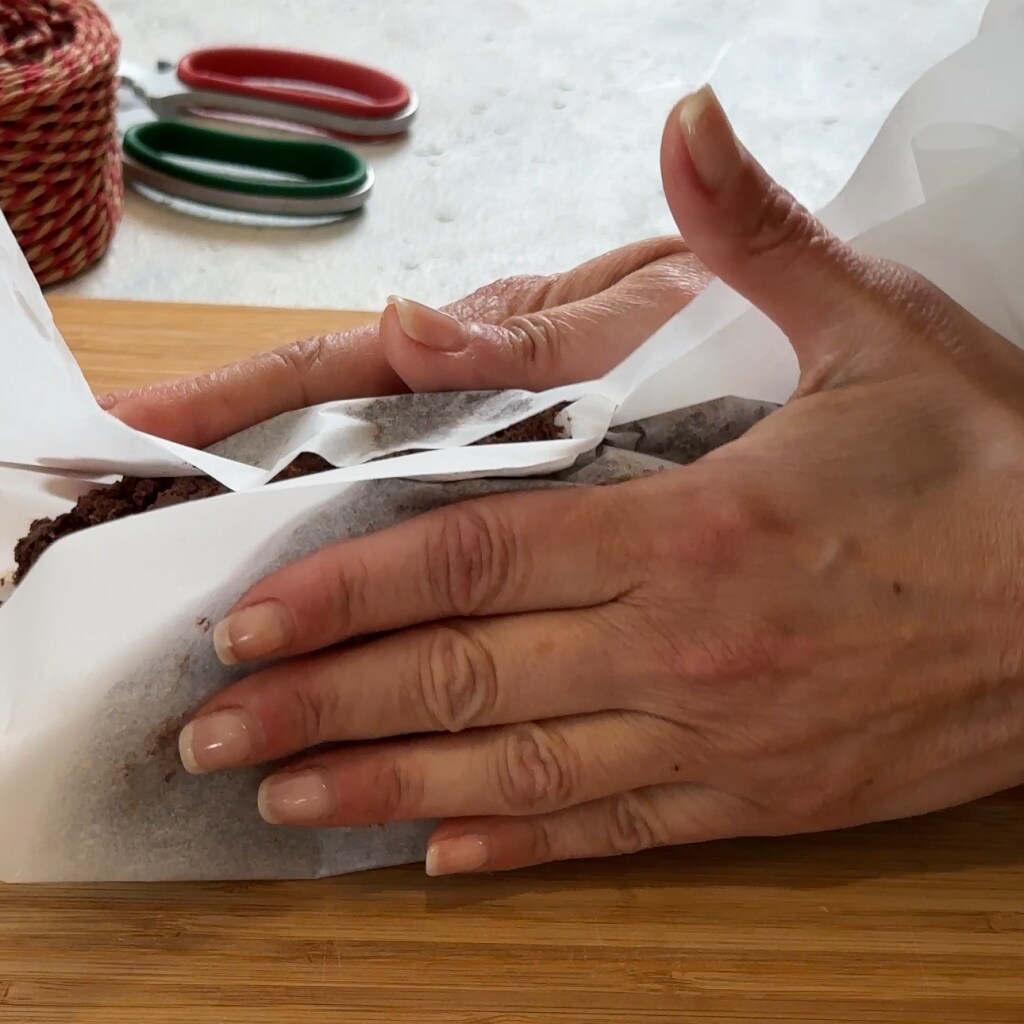 de vorm geven aan de chocoladesalami door met de handen het bakpapier samen te drukken